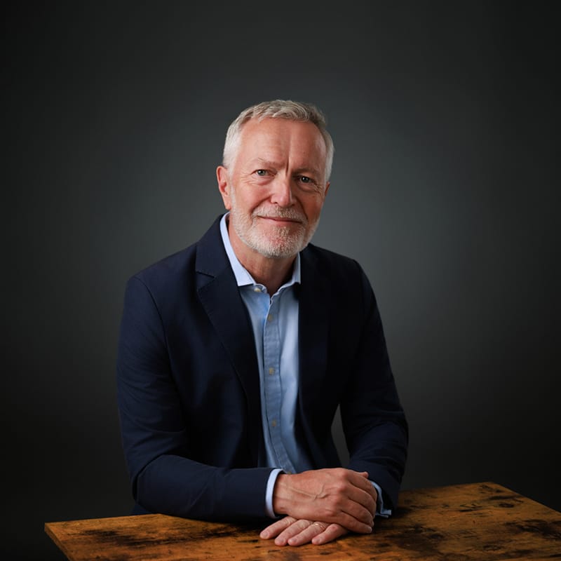 corporate headshot of man in blue suit sitting at table