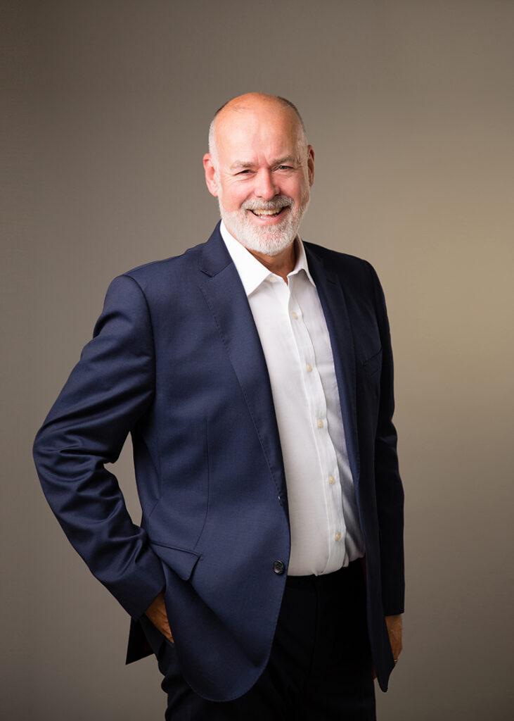 Studio portrait of a bearded male actor wearing a shirt and jacket against a neutral backdrop.