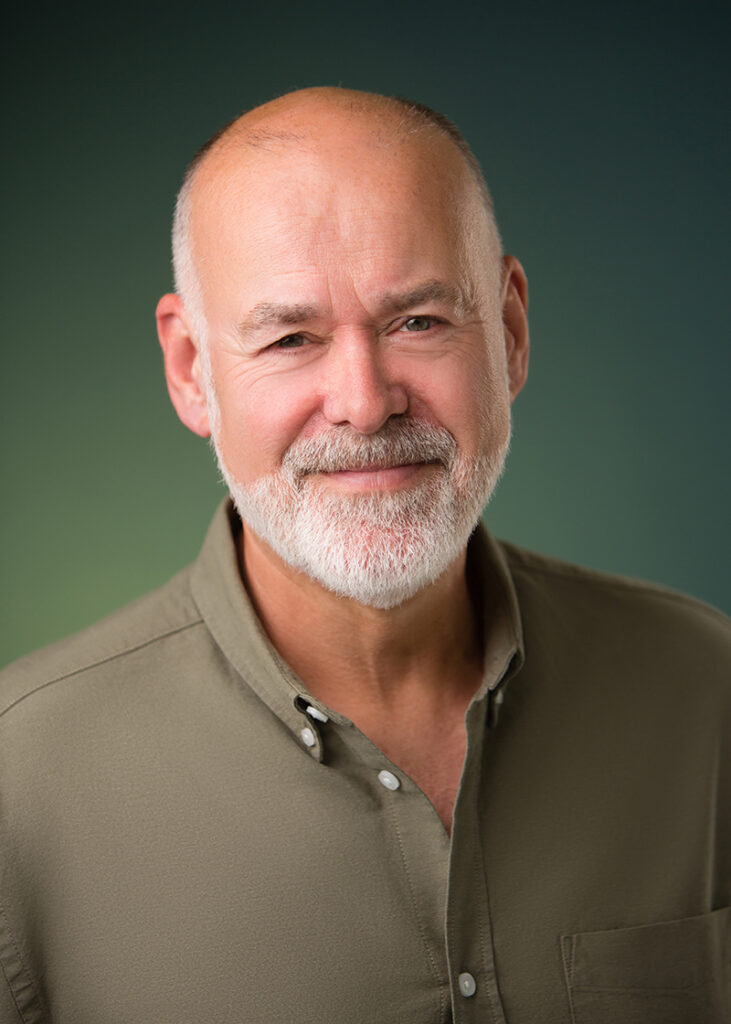 Studio headshot of a bearded man in relaxed shirt business and wam smiling expression.