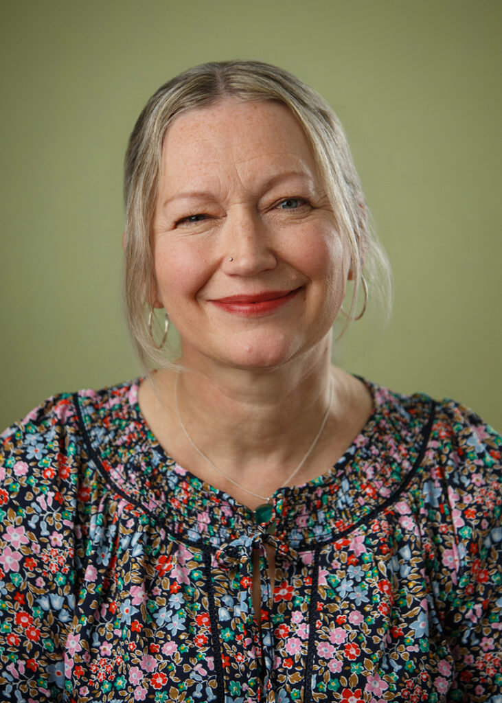 Studio headshot of a smiling woman on a warm green background.