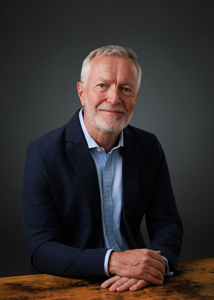 Studio headshot of a man in business attire with a relaxed, warm expression.